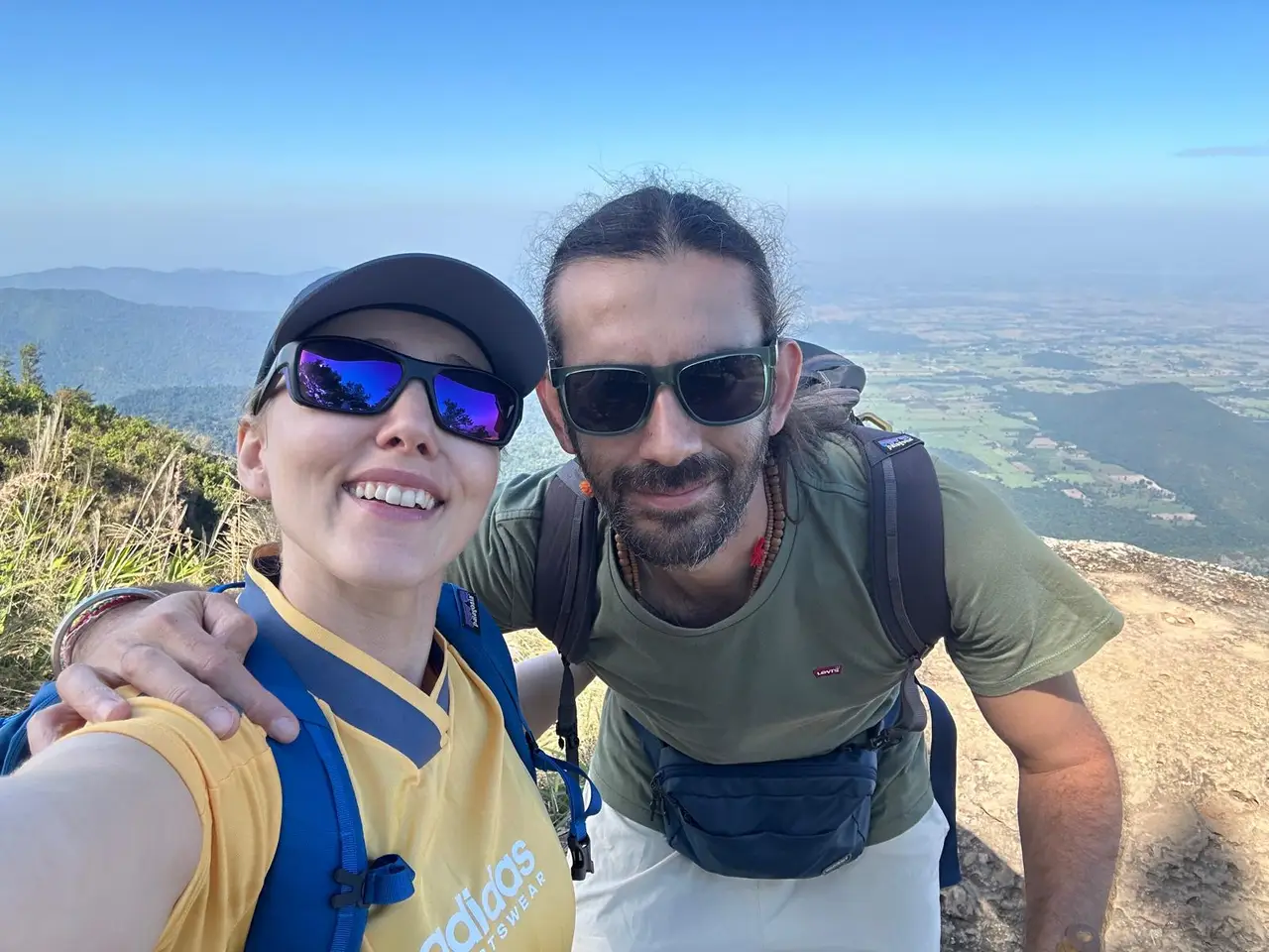 Paul and his wife smiling on a mountain summit, with valleys and farmland stretching out behind them